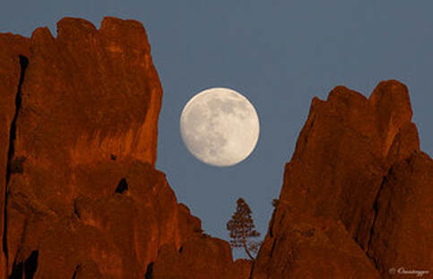 Moon captured between two rocky peaks in photo entitled Moonrise Over High Peaks by John Fox